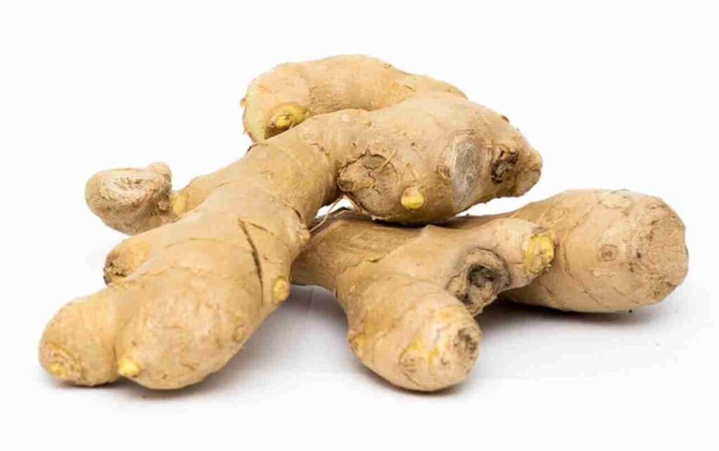 "A ginger root with slices and leaves on a wooden background."