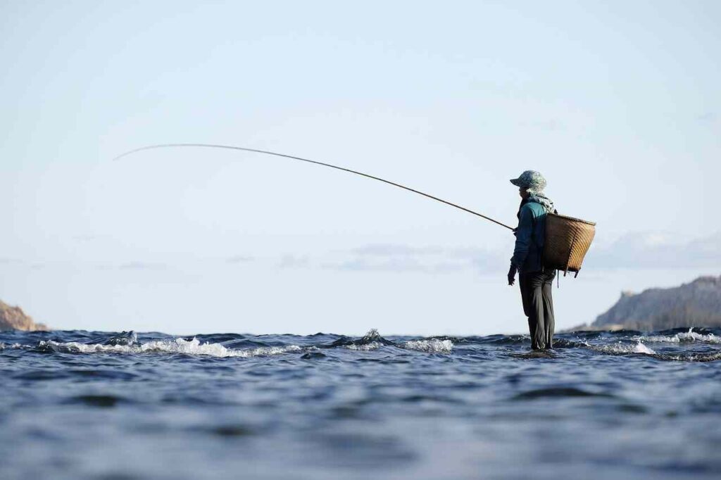 Person fishing by the lake on a sunny day, holding a fishing rod.