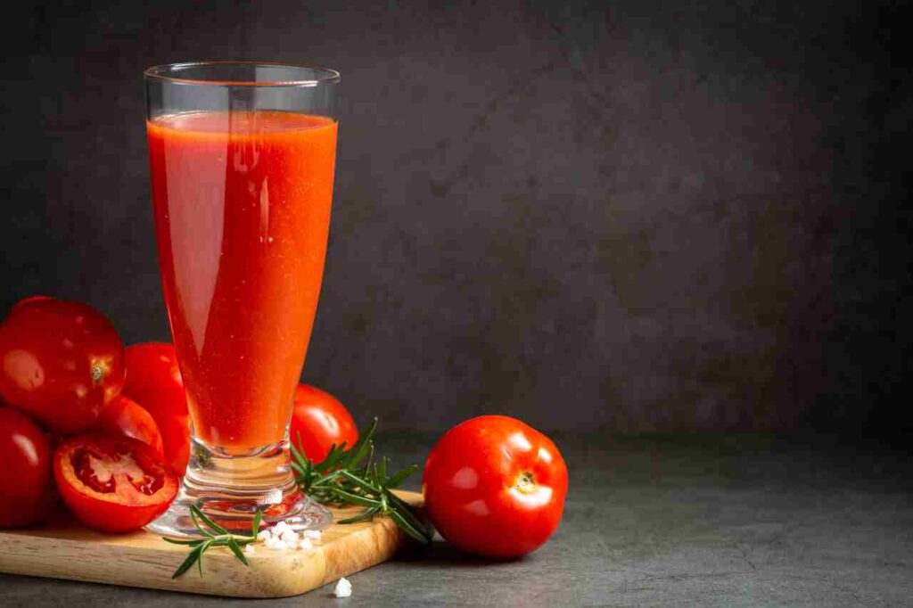 "Glass of tomato juice surrounded by fresh tomatoes on a table"