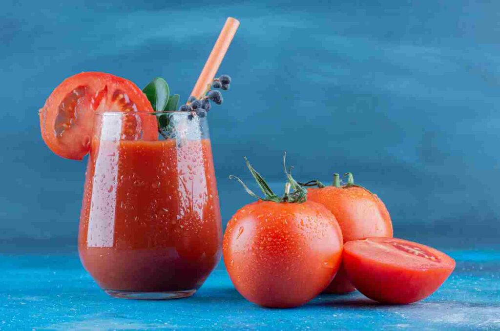 "Glass of tomato juice surrounded by fresh tomatoes on a table"